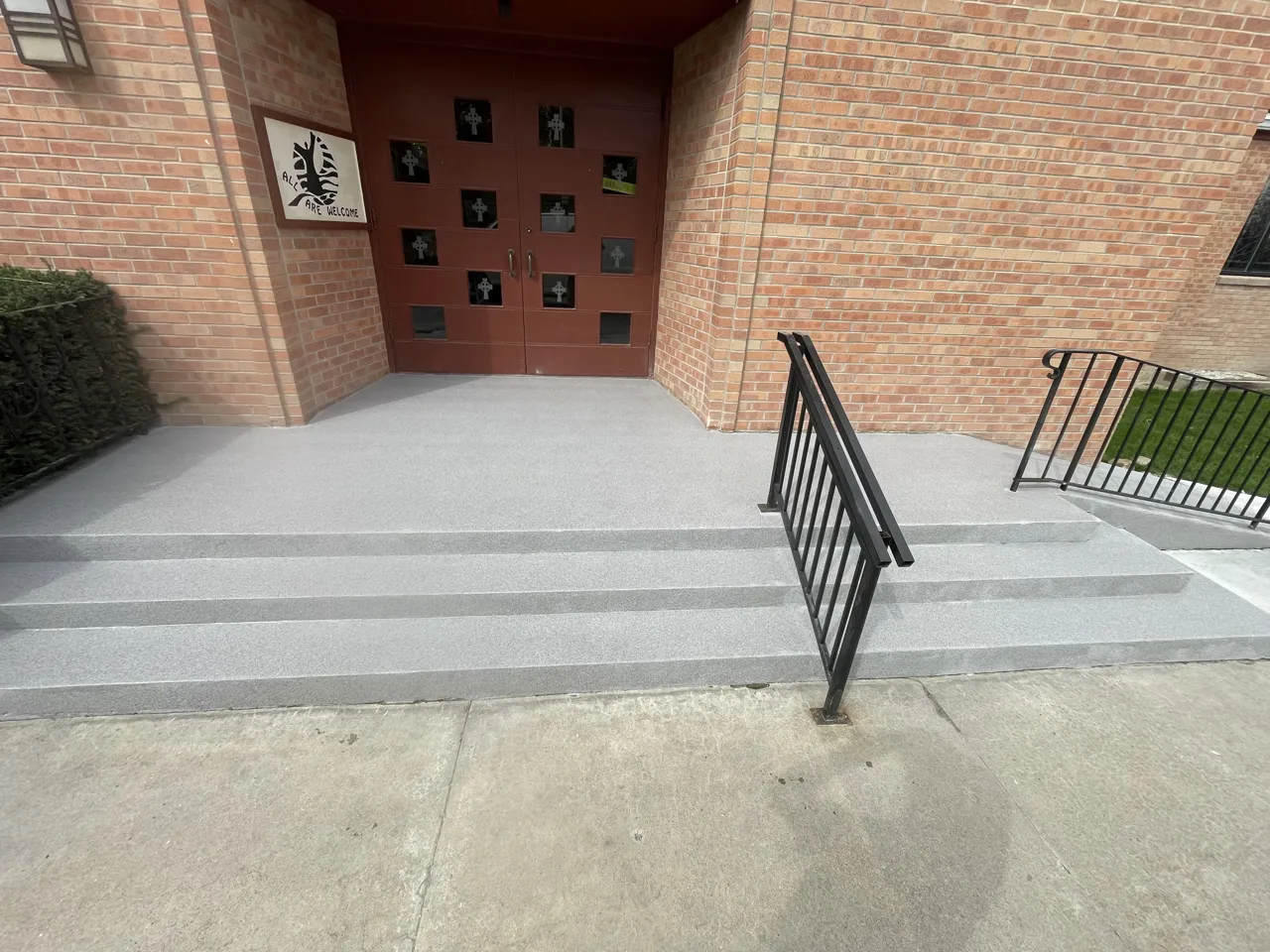 Gray coated entrance steps with black handrails beside a brick building