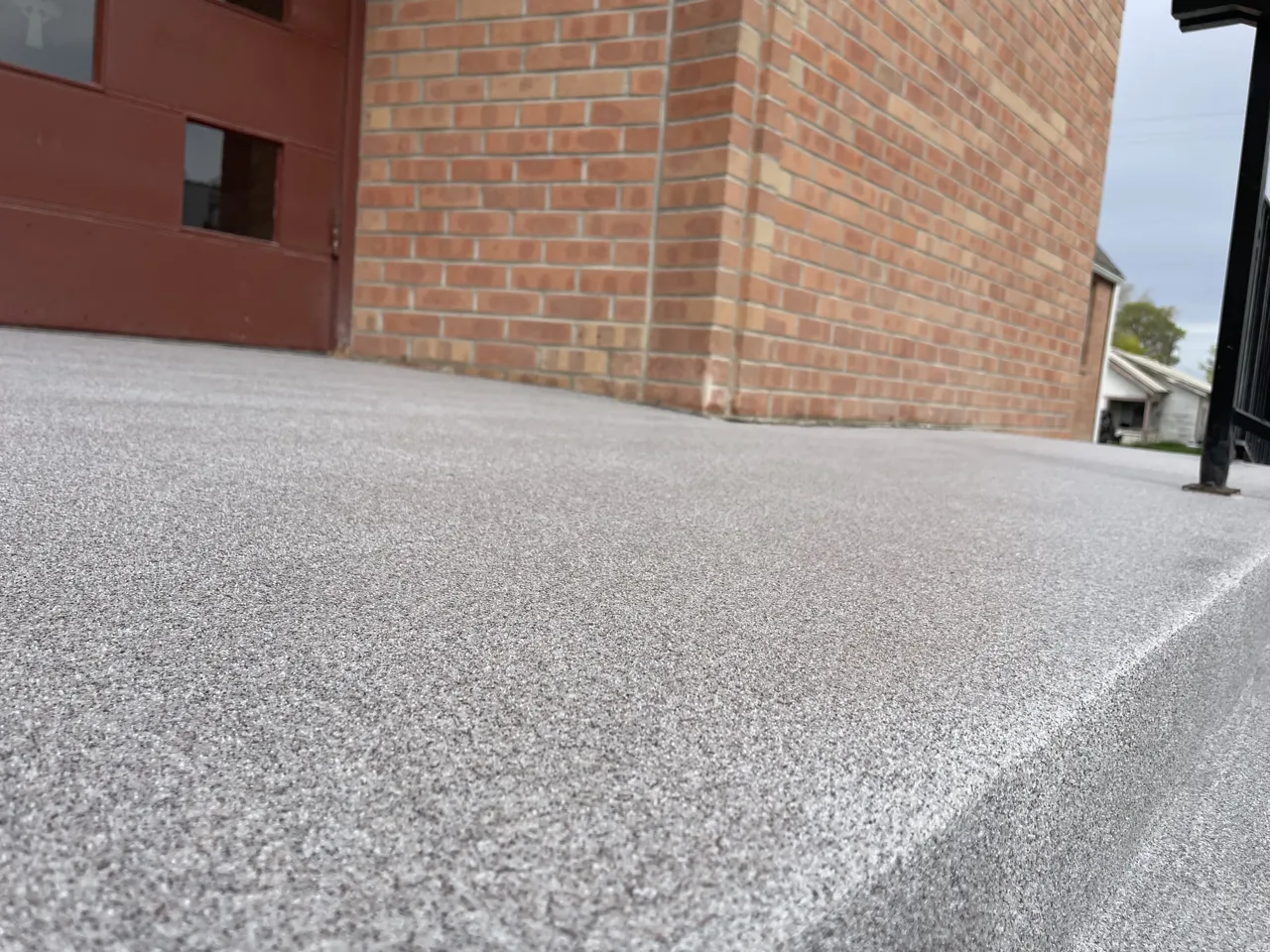Close view of a gray textured entrance landing beside brickwork